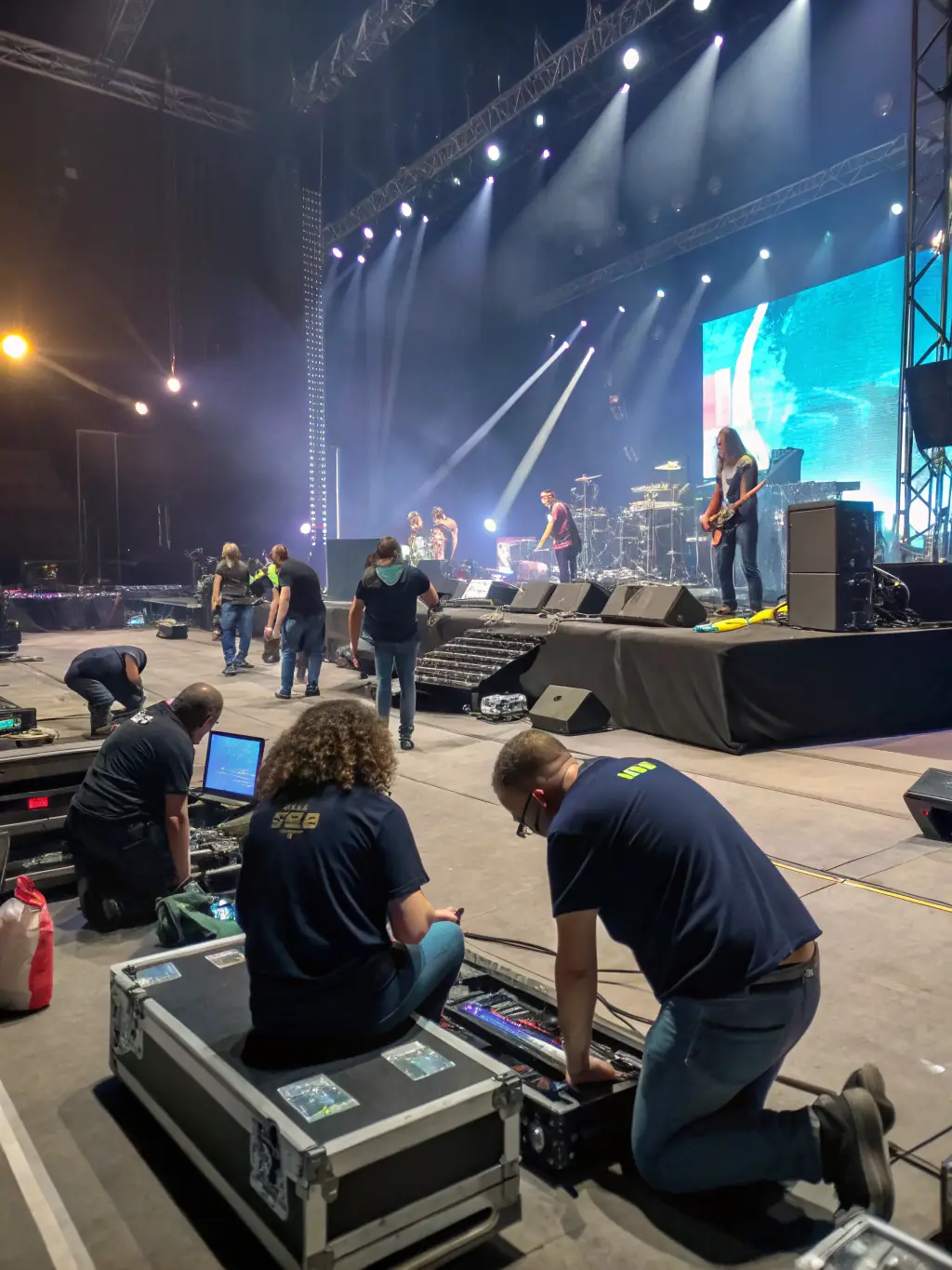 A photo of volunteers setting up equipment for an outdoor electronic music event organized by SECOND DEGRE. The scene shows teamwork and preparation, emphasizing the community involvement in making these events successful.